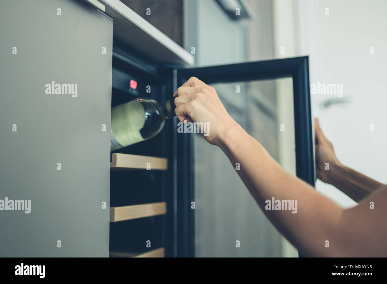 A young woman is getting a bottle of white wine from her wine cooler at home Stock Photo