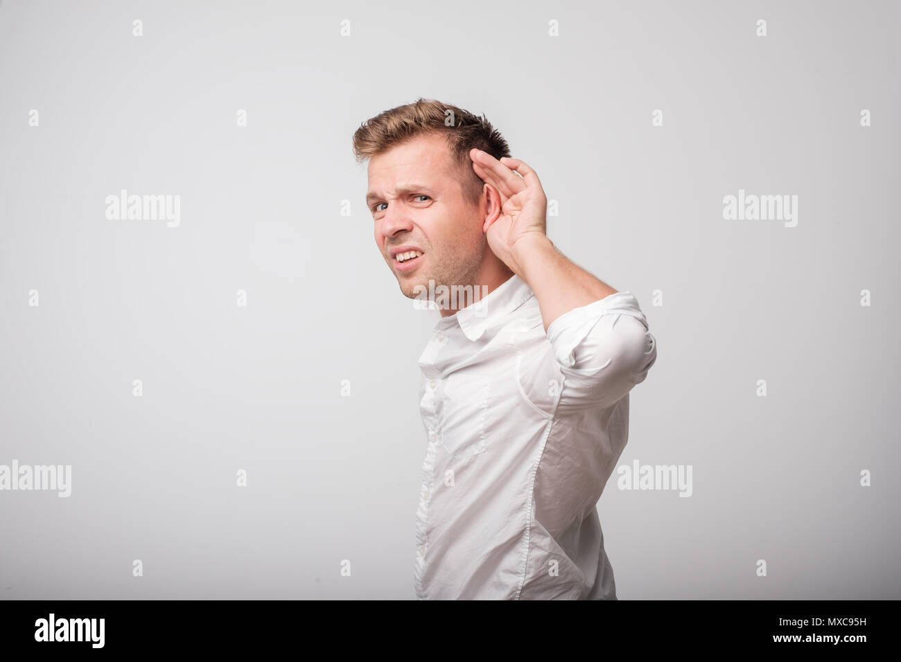 A young man puts a hand on the ear try to hear the whisper, isolated on a white background. Stock Photo