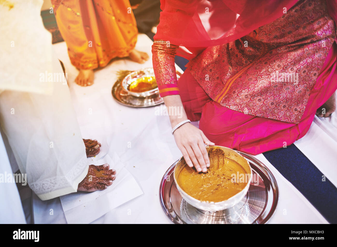 The bride standing on the white fabric and the women prepraing the turmeric (haldi) oil mixed with milk to pasting on the bride's feet and body, the t Stock Photo