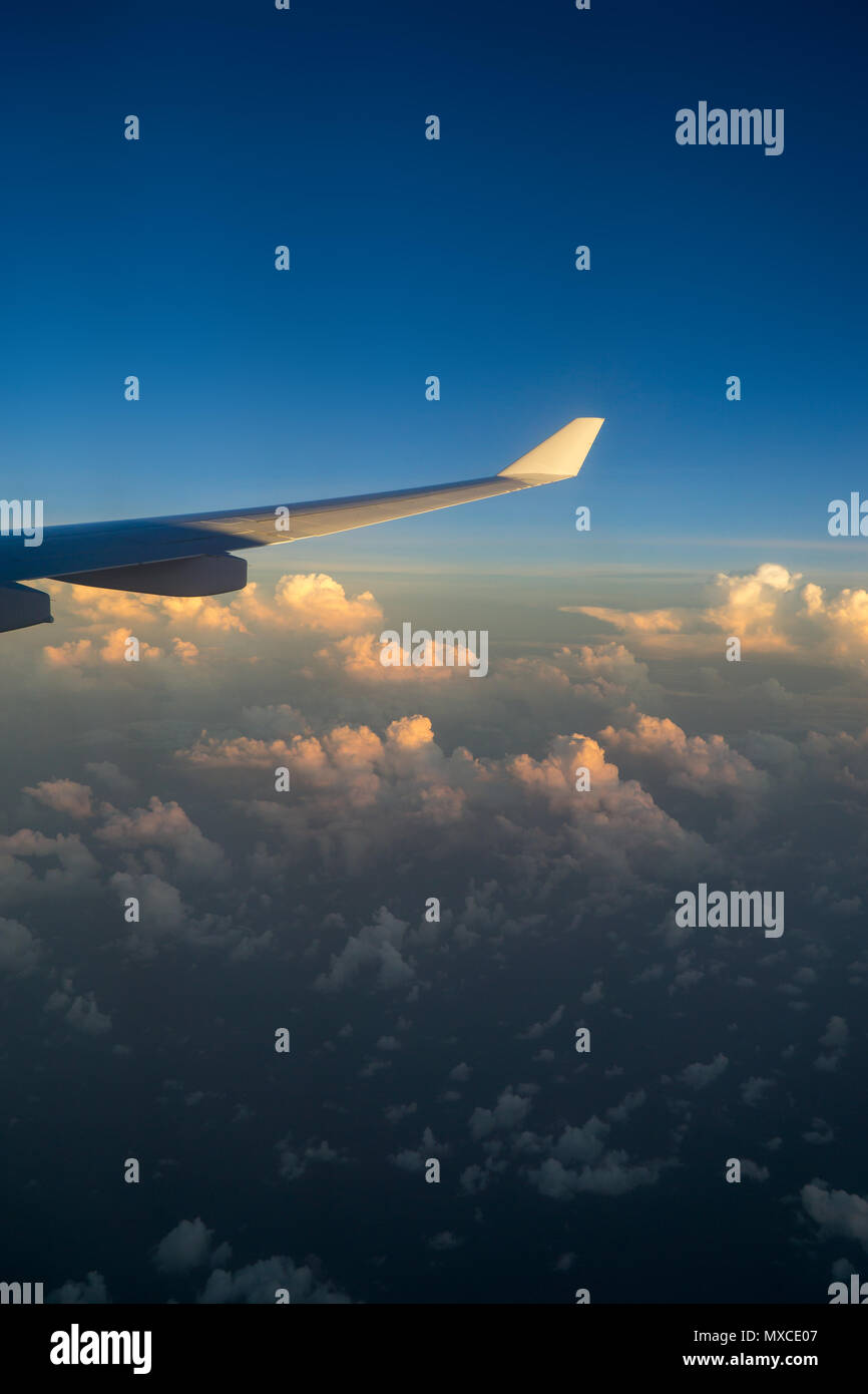 View out of airplane window with clouds at sunset and airplane wing. Stock Photo