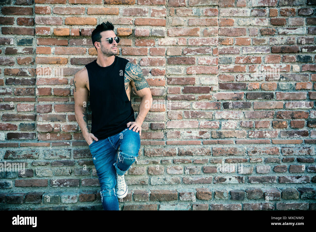 Muscular man leaning against old brick wall Stock Photo - Alamy