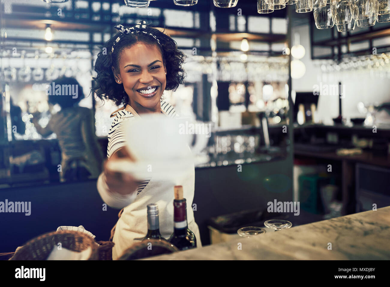 Young African barista smiling while standing behind the counter of a trendy cafe holding up a fresh cup of coffee Stock Photo