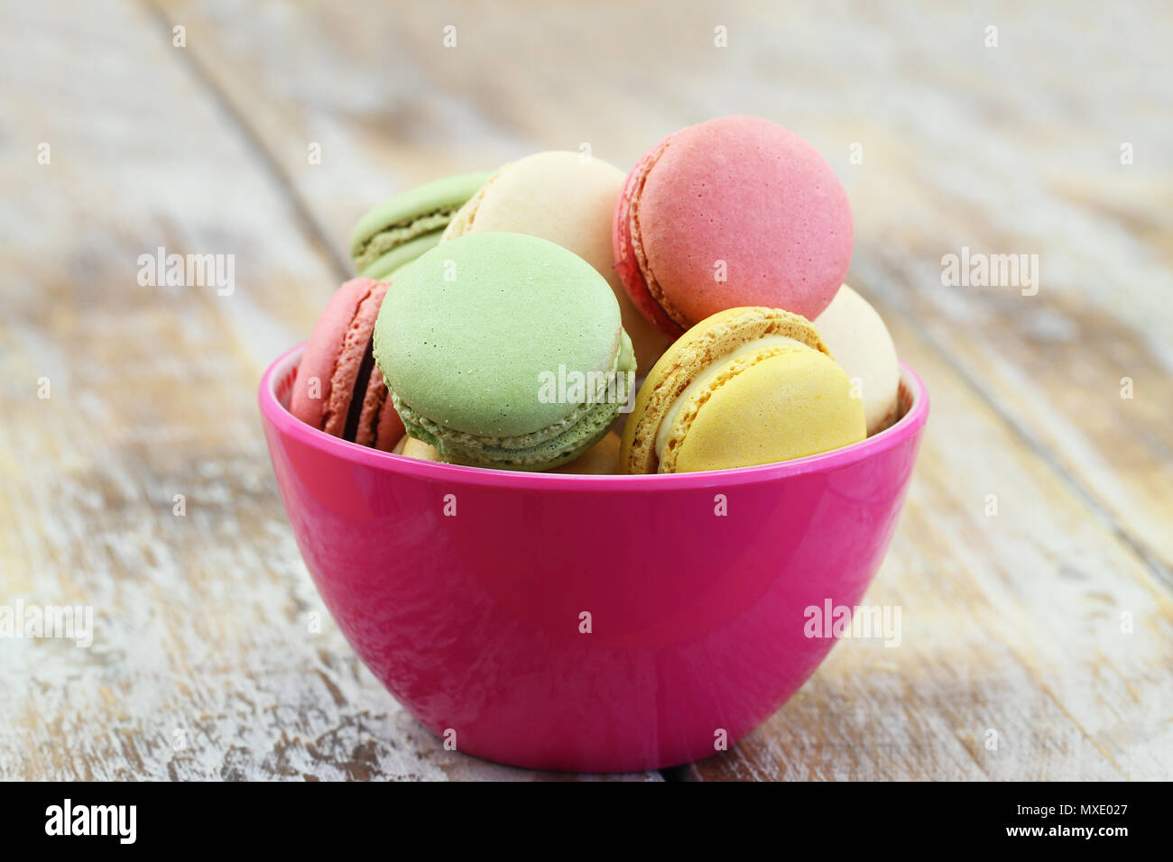 Colorful macaroons in pink bowl on rustic wooden surface with copy space Stock Photo