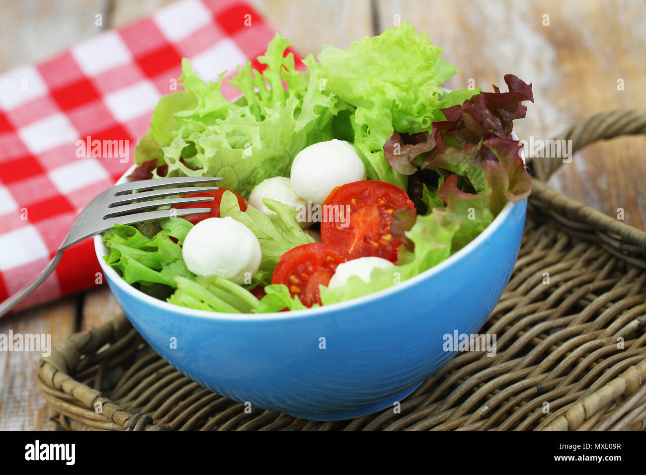 Fresh salad with mozzarella, lettuce and cherry tomatoes in blue bowl Stock Photo