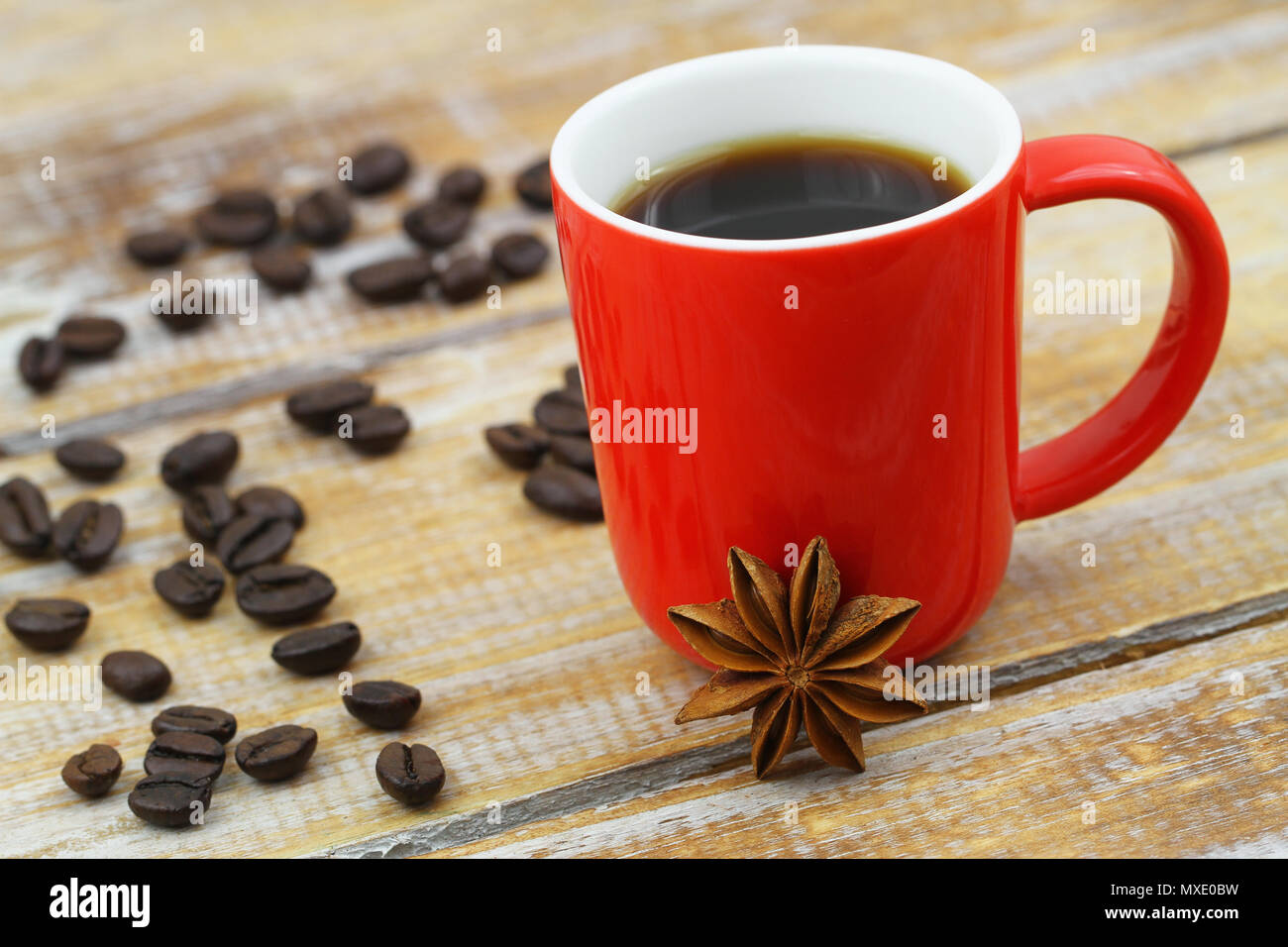 Star anise leaning against red mug of coffee on rustic wooden surface Stock Photo