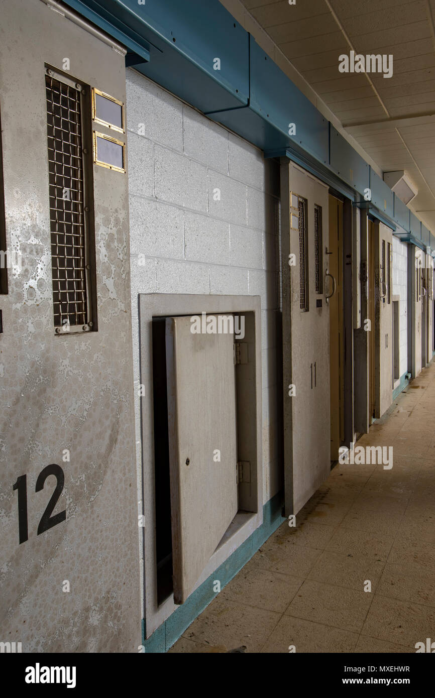 Row of numbered metal cell doors unlocked along hallway inside abandoned prison. Stock Photo