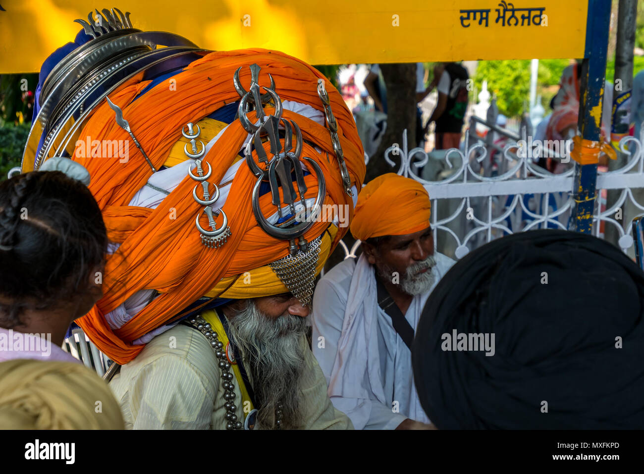 Sikh, with a huge turban on his head and religious symbols of the Sikh, sits surrounded by other men dressed in turbans. India July 2017 Stock Photo