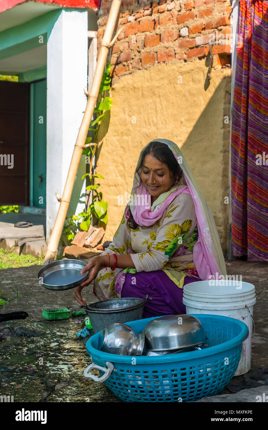 A woman in a traditional Indian dress washes dishes in front of her house in the countryside. India July 2015 Stock Photo