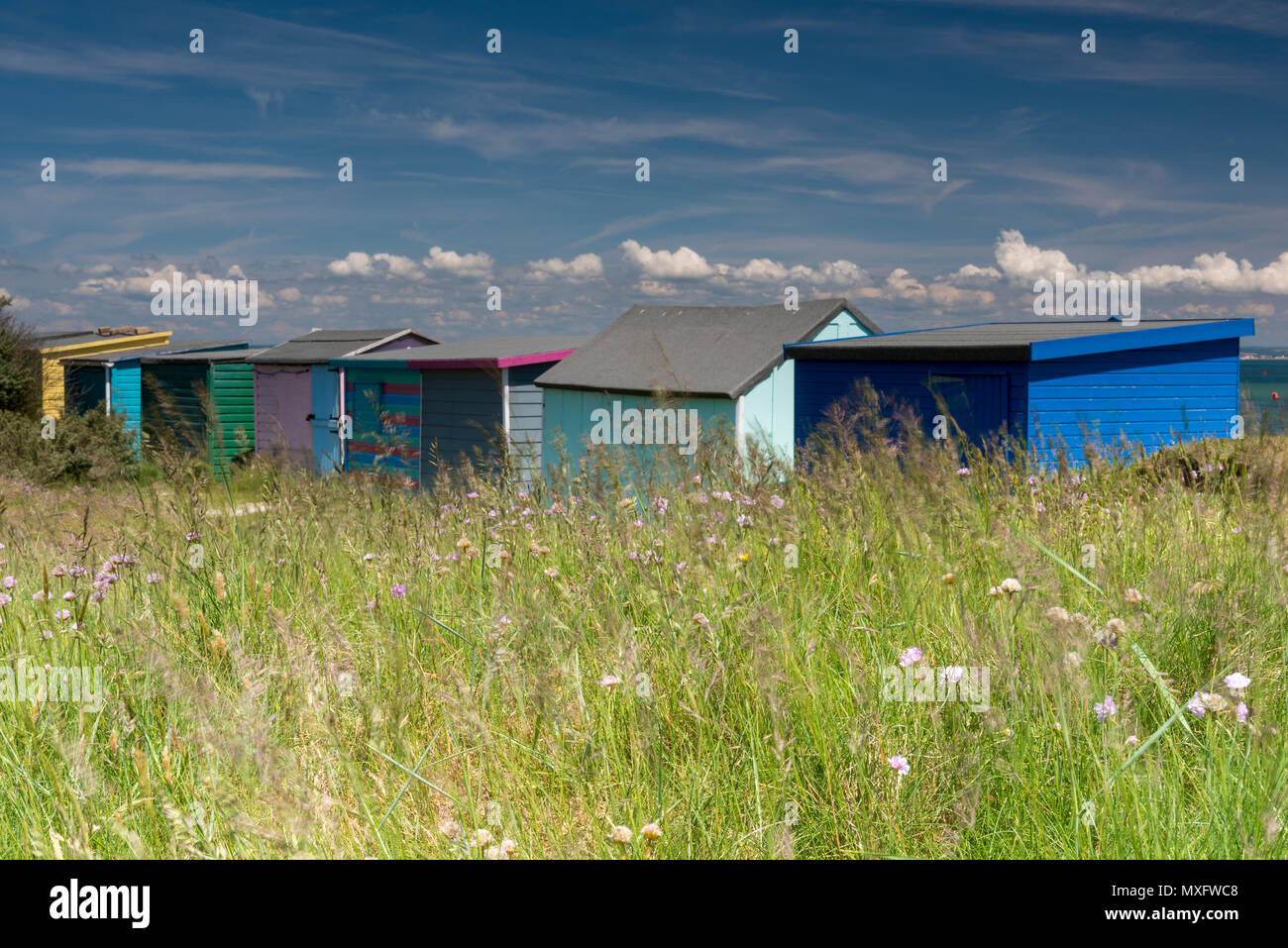 A row of brightly coloured beach huts at bembridge duvet on the Isle of Wight with an interesting cloud formation above on a hot weather summers day. Stock Photo