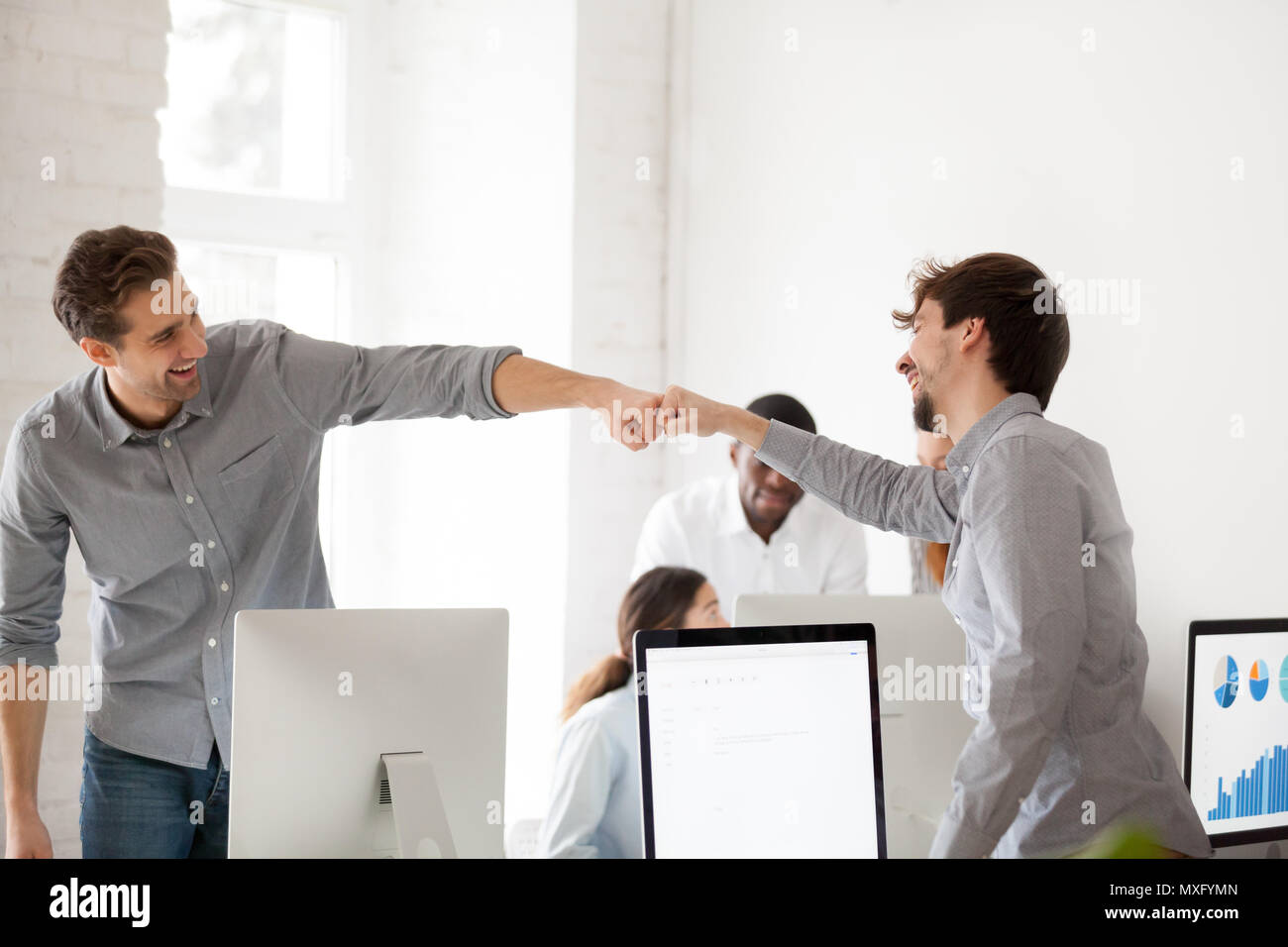 Smiling males giving fist bumps excited by shared goal achieveme Stock Photo