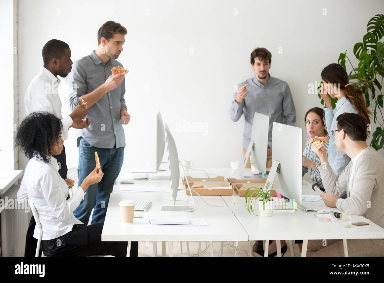 Multinational work group talking and eating pizza at workplace Stock Photo