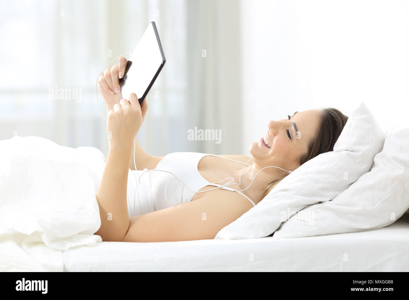 Happy girl watching tv online with a tablet and earphones in the bed at home Stock Photo Alamy