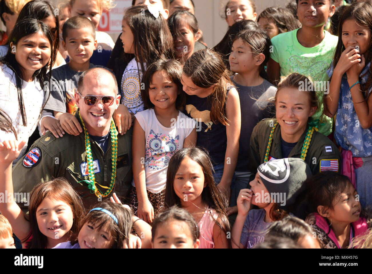 Lt. Cmdr. Roger Barr, left, and Lt. Lisa Davis, right, both MH-65 Dolphin helicopter pilots assigned to Coast Guard Air Station Barbers Point, take a photo with local children during a career day at Lanai High and Elementary School in Lanai, Nov. 2, 2016. (U.S. Coast Guard photo by Petty Officer 2nd Class Tara Molle) Stock Photo