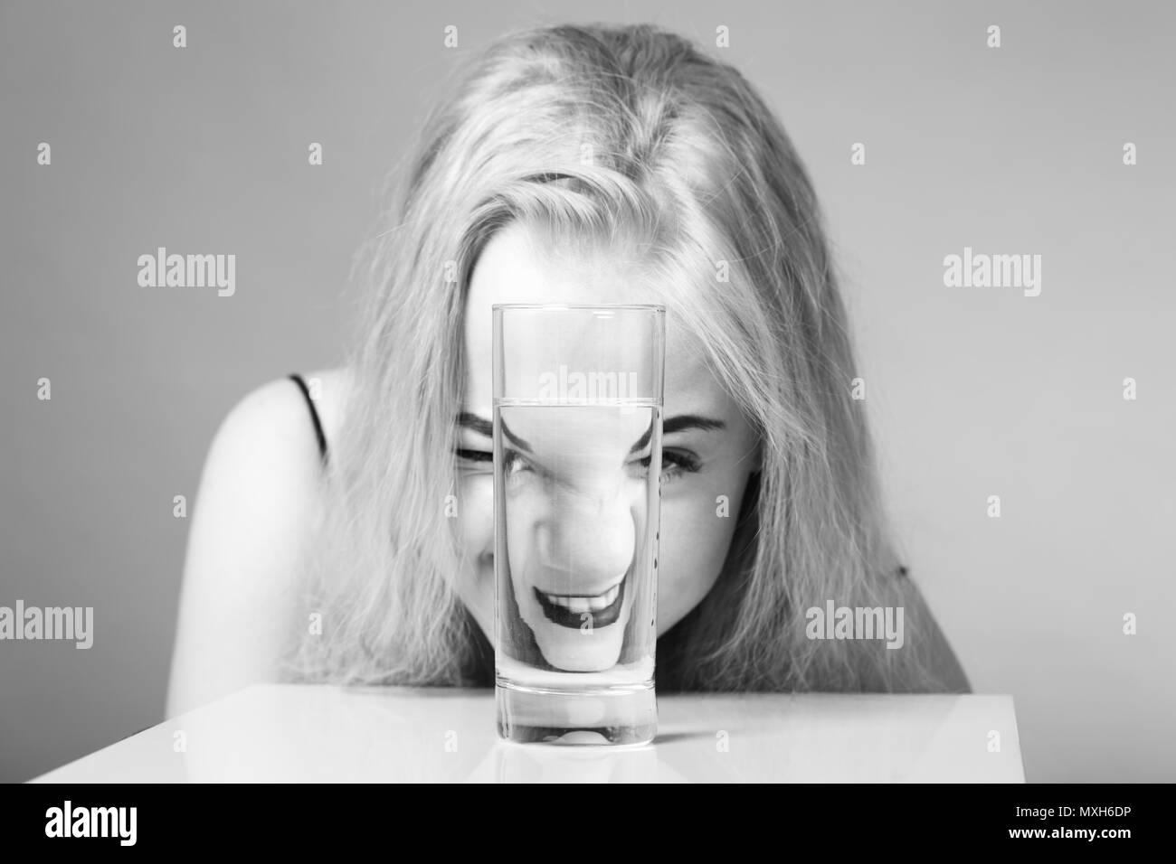 girl looks at camera through glass with water on gray background, laughing, monochrome Stock Photo