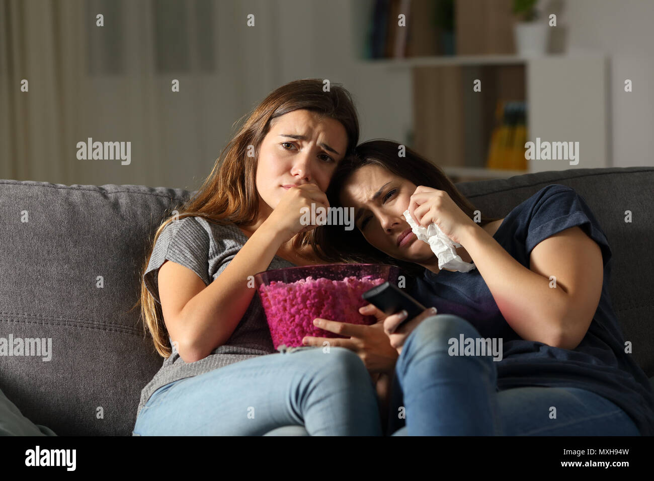 Two sad friends crying watching tv in the night sitting on a couch in the living room at home Stock Photo