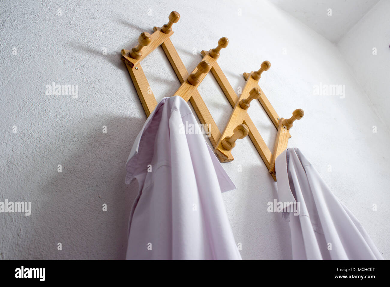 A wood wall cloth hanger with two white shirts in it. It hangs in the laundry of a small domestic house. Stock Photo