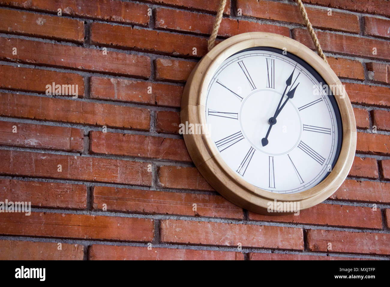 Medium close shot of a wooden wall clock with roman numerals hanging in a red brick wall. Stock Photo