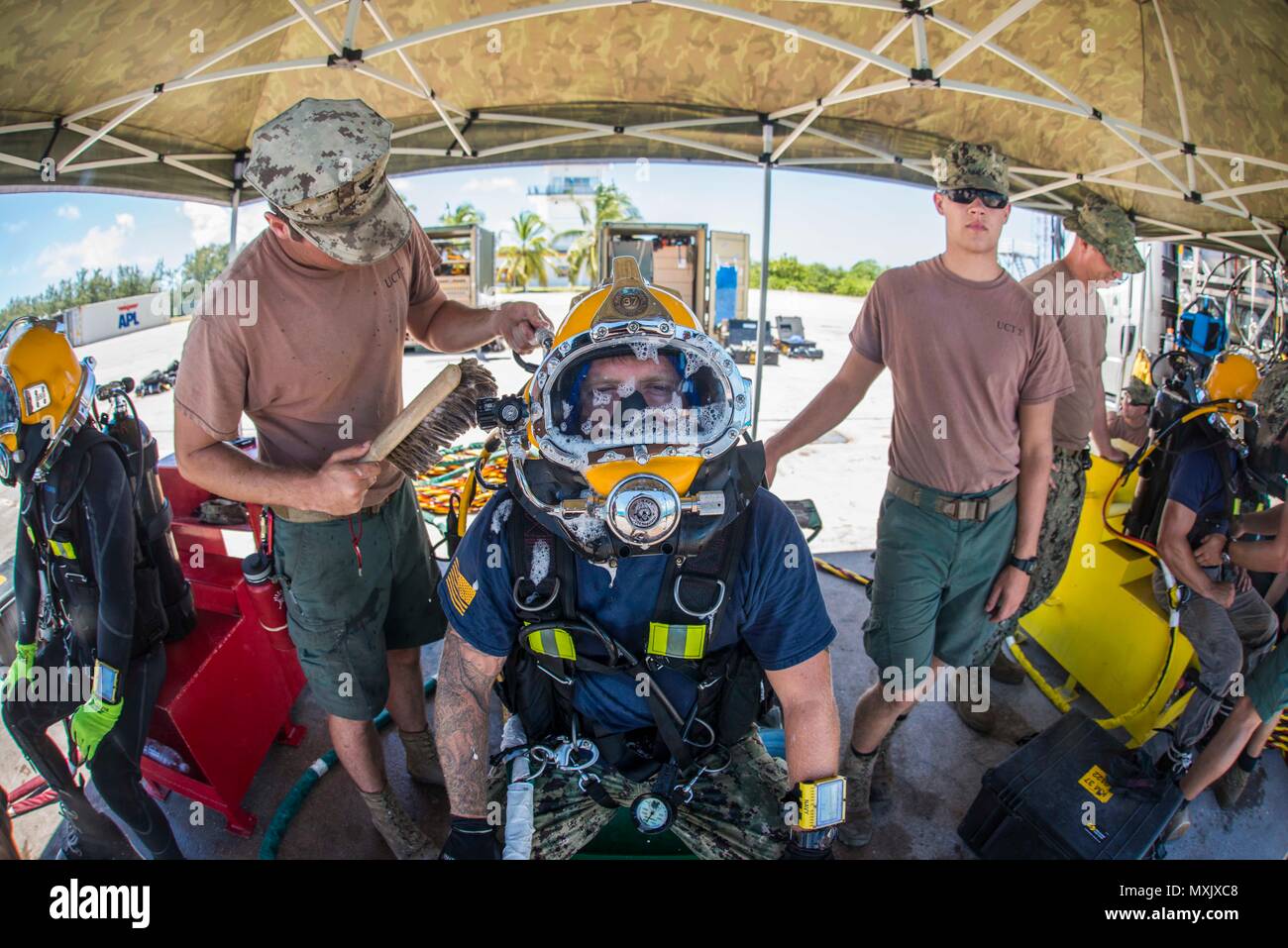 Petty Officer 2nd Class Aaron Brown, center, assigned to Underwater Construction Team (UCT) 2’s Construction Dive Detachment Bravo (CDDB),  has his KM-37 diving helmet checked for leaks in Diego Garcia, British Indian Ocean Territory, Nov. 8, 2016.  CDDB is performing precision underwater demolition and light salvage to remove obstructions from Diego Garcia's deep draft wharf. CDDB is on the third stop of their deployment, where they are conducting inspection, maintenance, and repair of various underwater and waterfront facilities while under Commander, Task Force (CTF) 75, the primary expedit Stock Photo