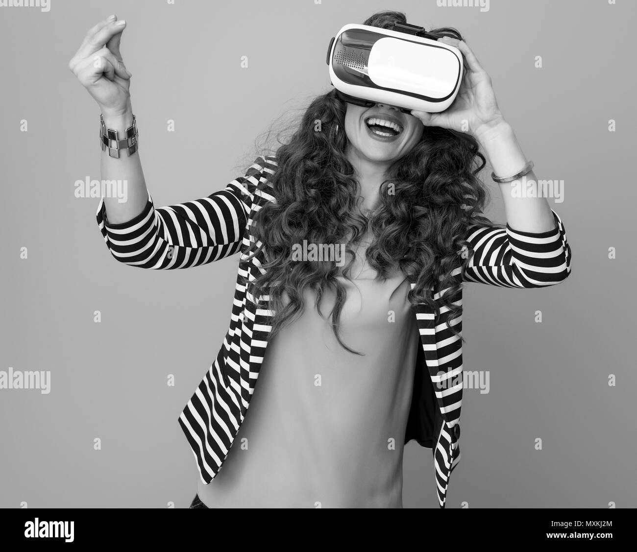 happy stylish woman with long wavy brunette hair against background using virtual reality gear and snapping fingers Stock Photo
