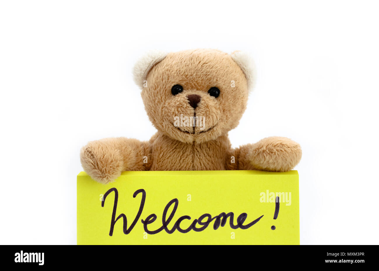 Brown teddy bear holding with the two hands a note in bright yellow color with the handwritten message “Welcome!” as welcome sign concept. Photo isola Stock Photo