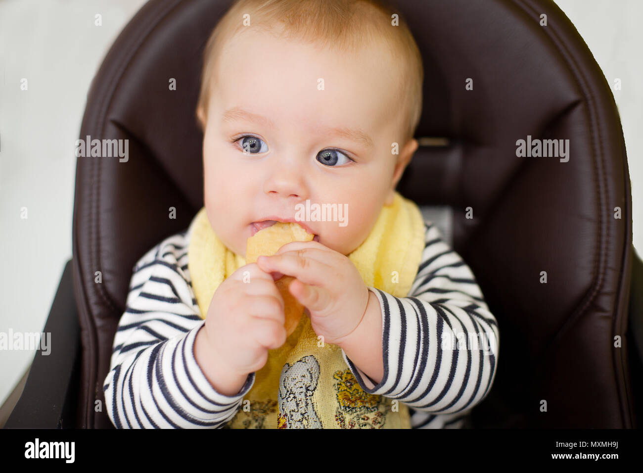 little baby boy sitting in chair for feeding and eating special biscuit