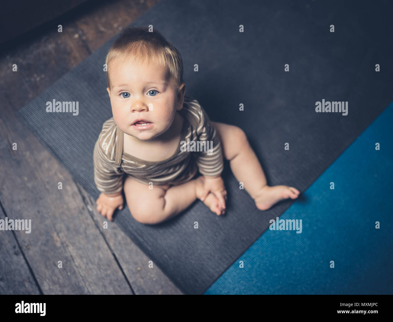 A little baby is sitting on some yoga mats on the floor Stock Photo Alamy