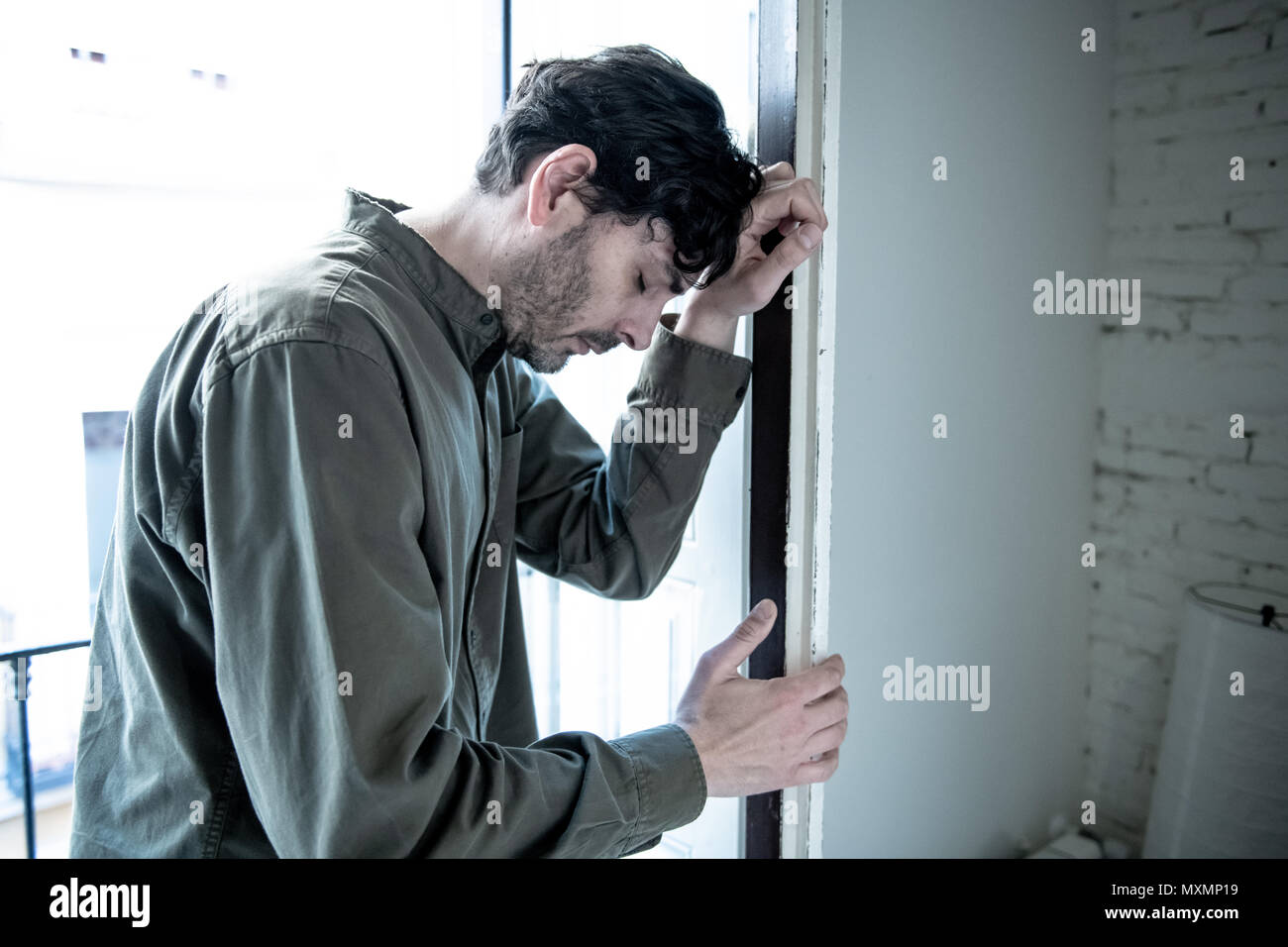 Lonely young man looking outside house balcony looking depressed, destroyed, sad and suffering emotional crisis and grief thinking of taking a difficu Stock Photo