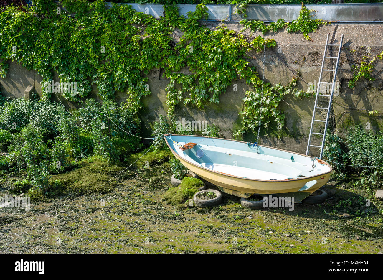 A boat is beached on the muddy river bed during low tide on The River Thames. Stock Photo