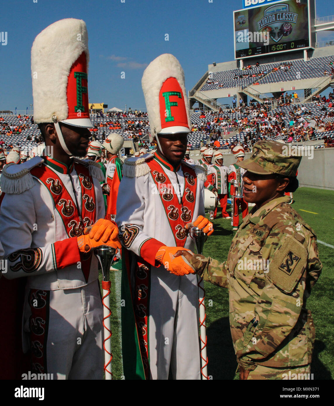 Minutes before the opening kickoff of the 2016 Florida Classic, Army Master Sgt. Shantell D. Aviles, noncommissioned officer-in-charge, Office of the Inspector General, 143d Sustainment Command (Expeditionary), shakes hands with two drum majors from the Florida A&M University marching band Nov. 19, 2016, at Camping World Stadium in Orlando, Fla. Aviles, a native of Rockledge, Fla., grew up watching the Florida Classic. Although she and her family are no strangers to seeing the game from the stands, Aviles had never before set foot on the sidelines. With a smile never left her face, she took fu Stock Photo