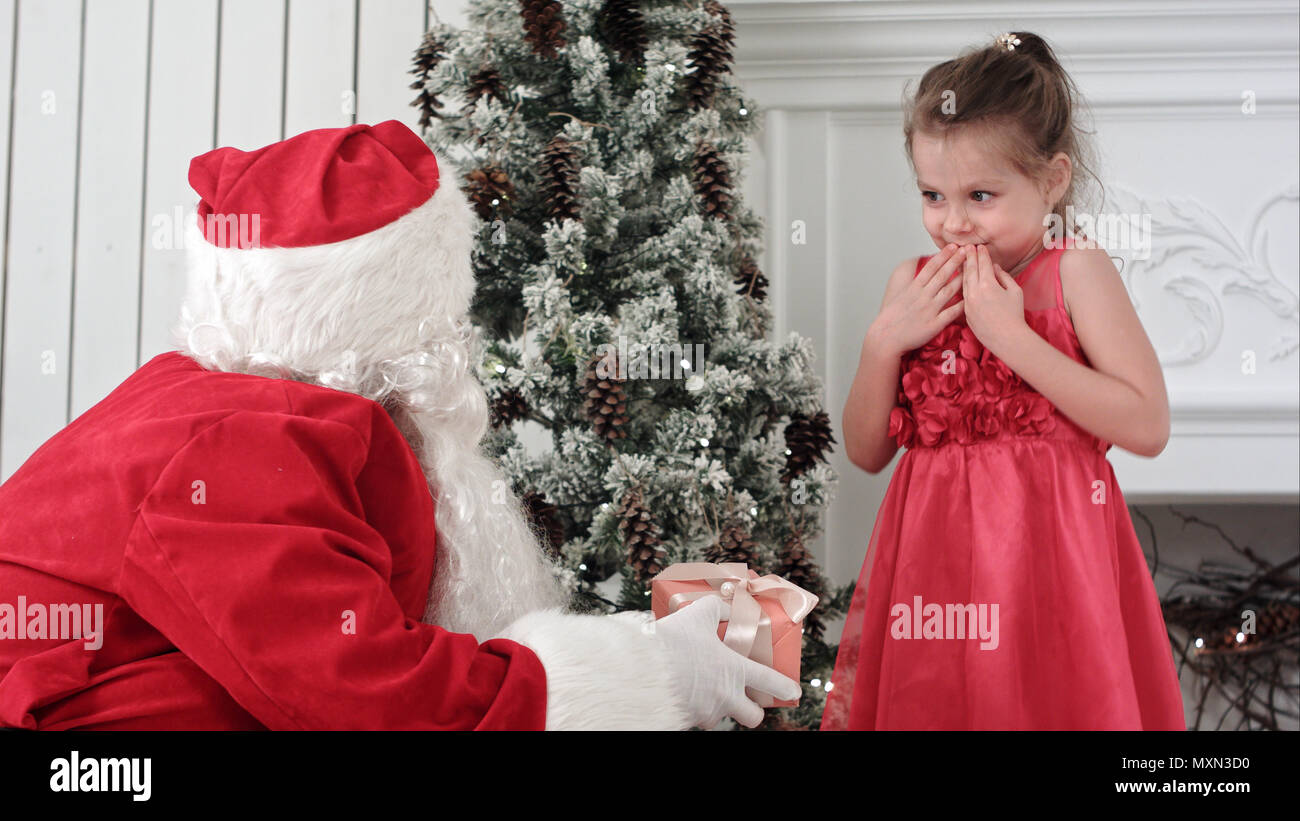 Santa Claus giving present to a surprised little girl and hugging her ...