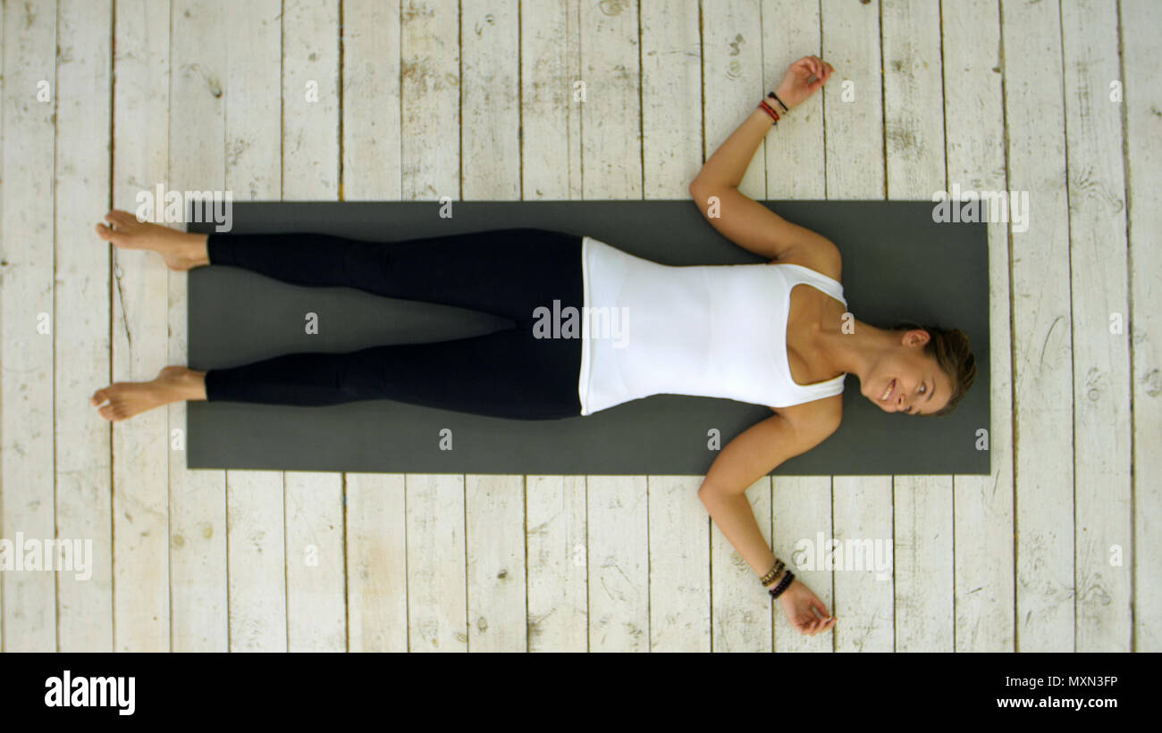 Attractive young woman working out at home, doing yoga exercise, lying in Shavasana Corpse or Dead Body Pose , resting after practice, meditating, breathing Stock Photo