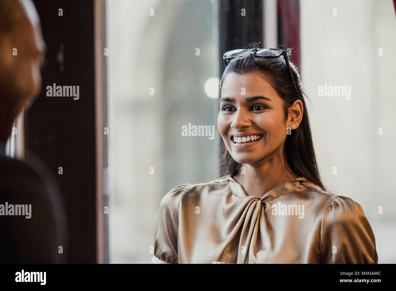 Over the shoulder view of a smiling businesswoman talking to an unrecognisable person. Stock Photo
