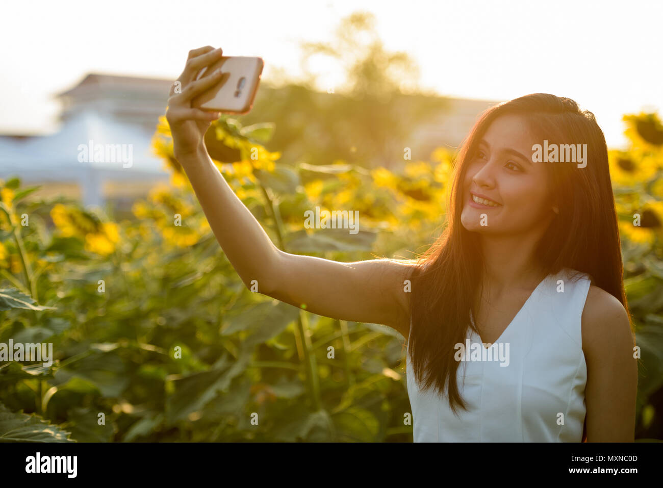 Young happy Asian woman smiling while taking selfie picture with Stock Photo