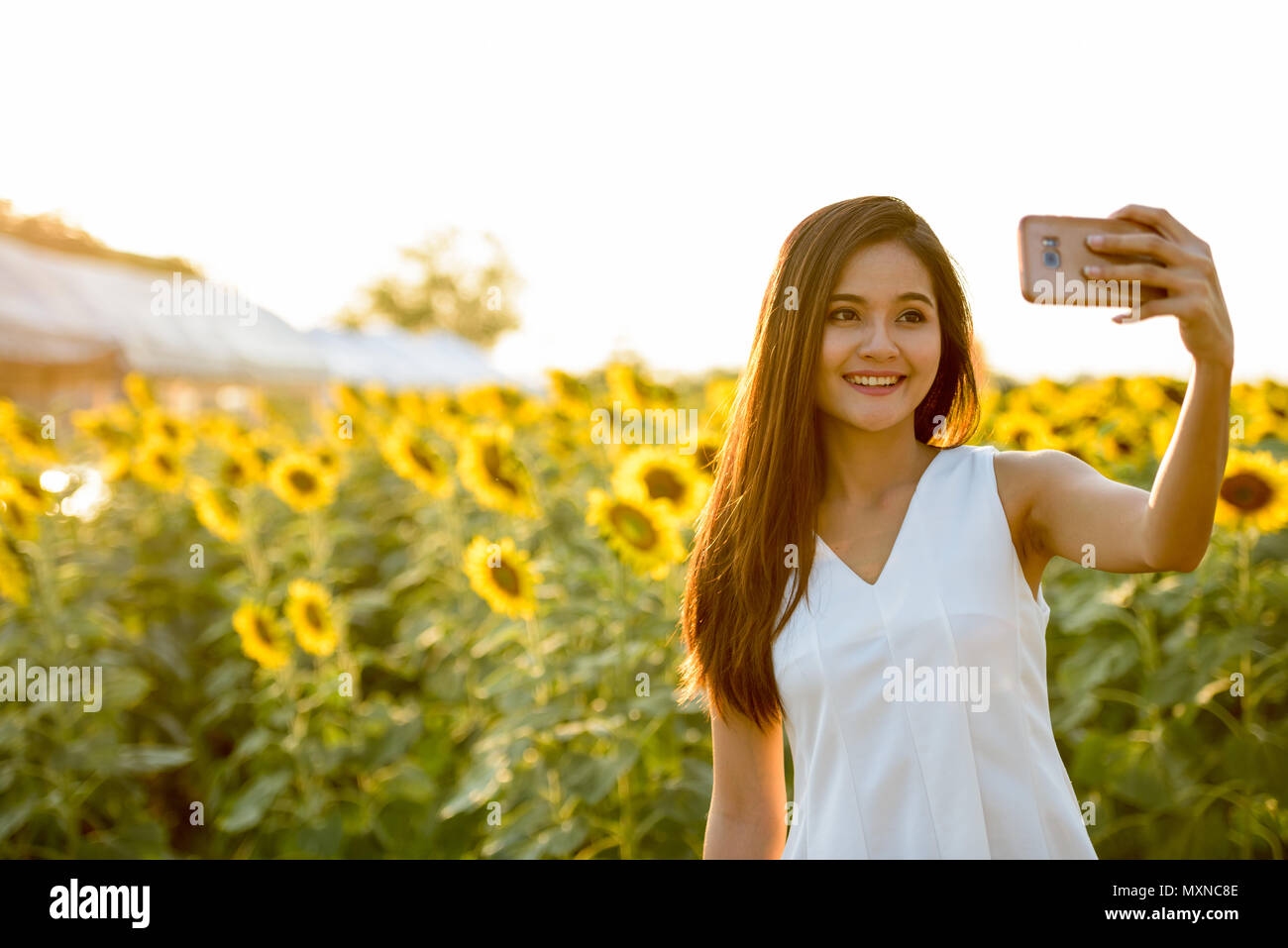 Young happy Asian woman smiling while taking selfie picture with Stock Photo