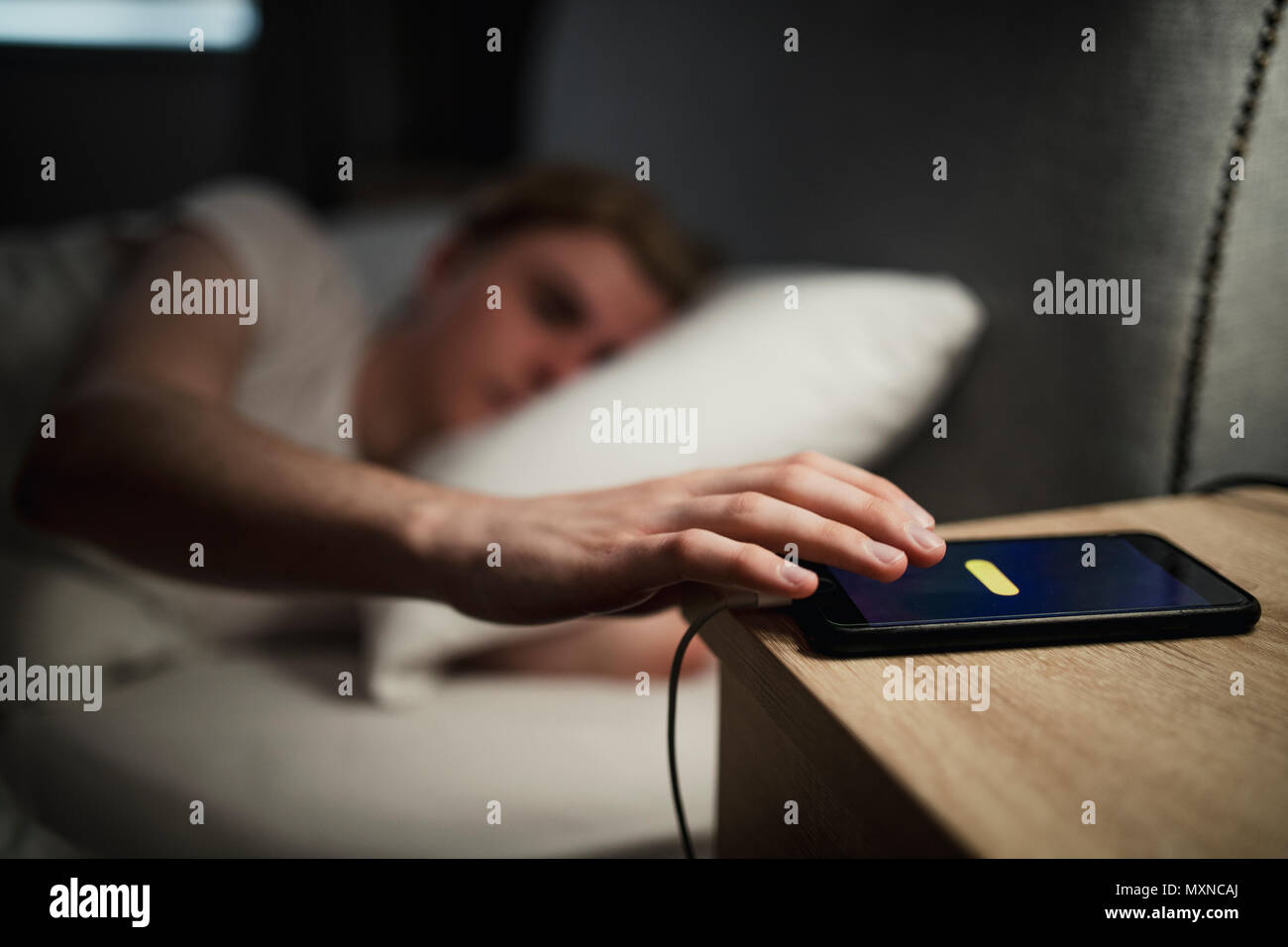 Young adult male struggling on a morning to wake up, hitting snooze on his alarm. Stock Photo