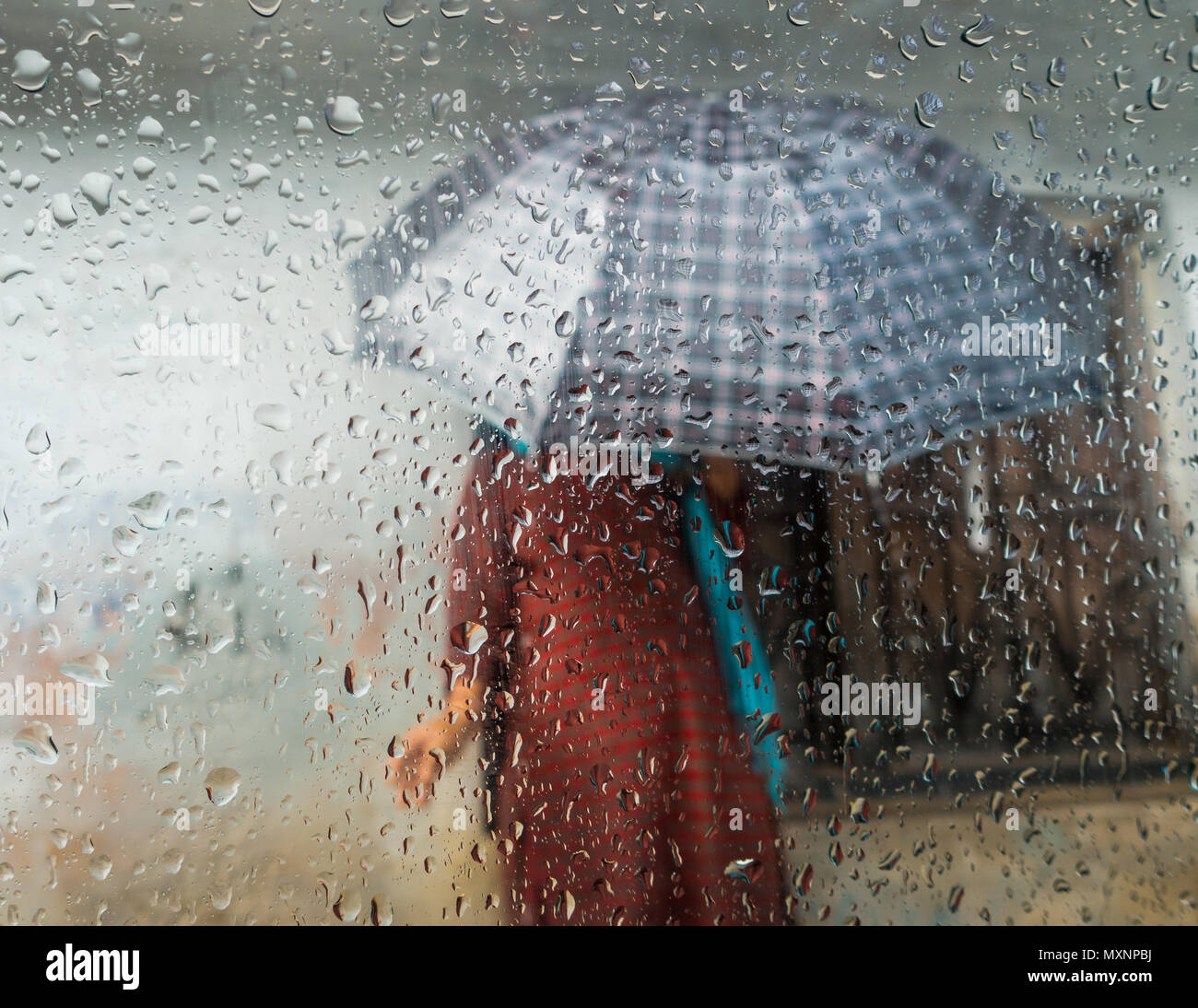 Monsoon season in Kathmandu, Nepal. Woman holding an umbrella seen through a window. Focus on droplets on glass. Stock Photo