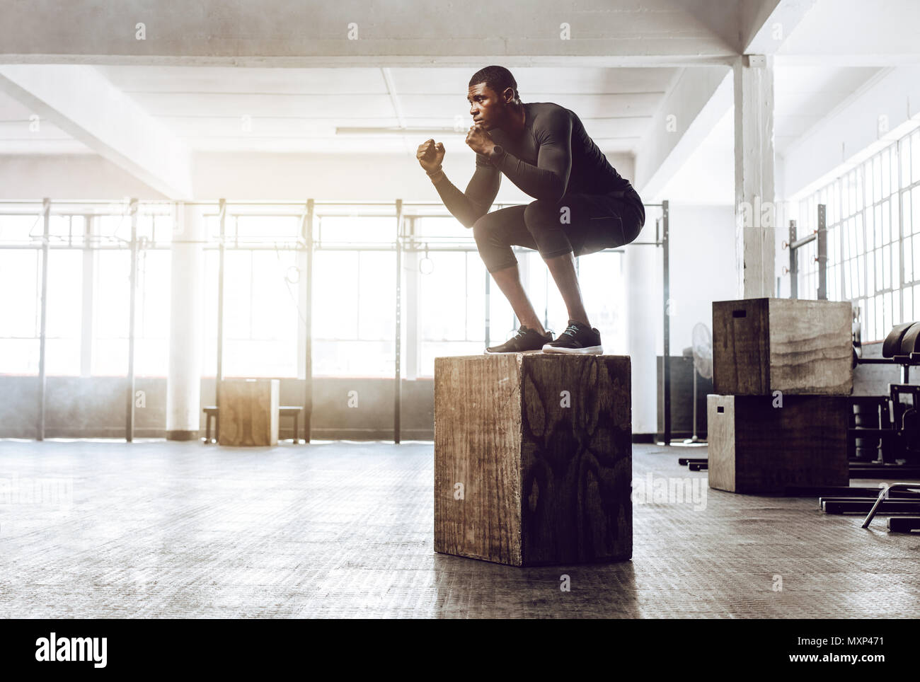 Man doing squats on a squat box at the gym. Crossfit guy at the gym working out standing on a wooden squat box. Stock Photo