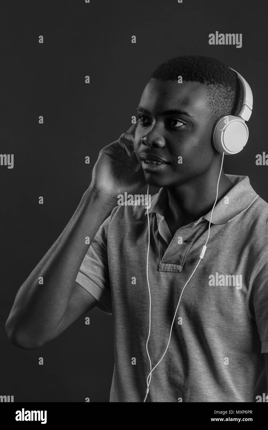 Close up portrait of dark skinned man with closed eyes, has headphones, listens to favourite music. Teenager enjoys audio track isolated on white gray wall Stock Photo