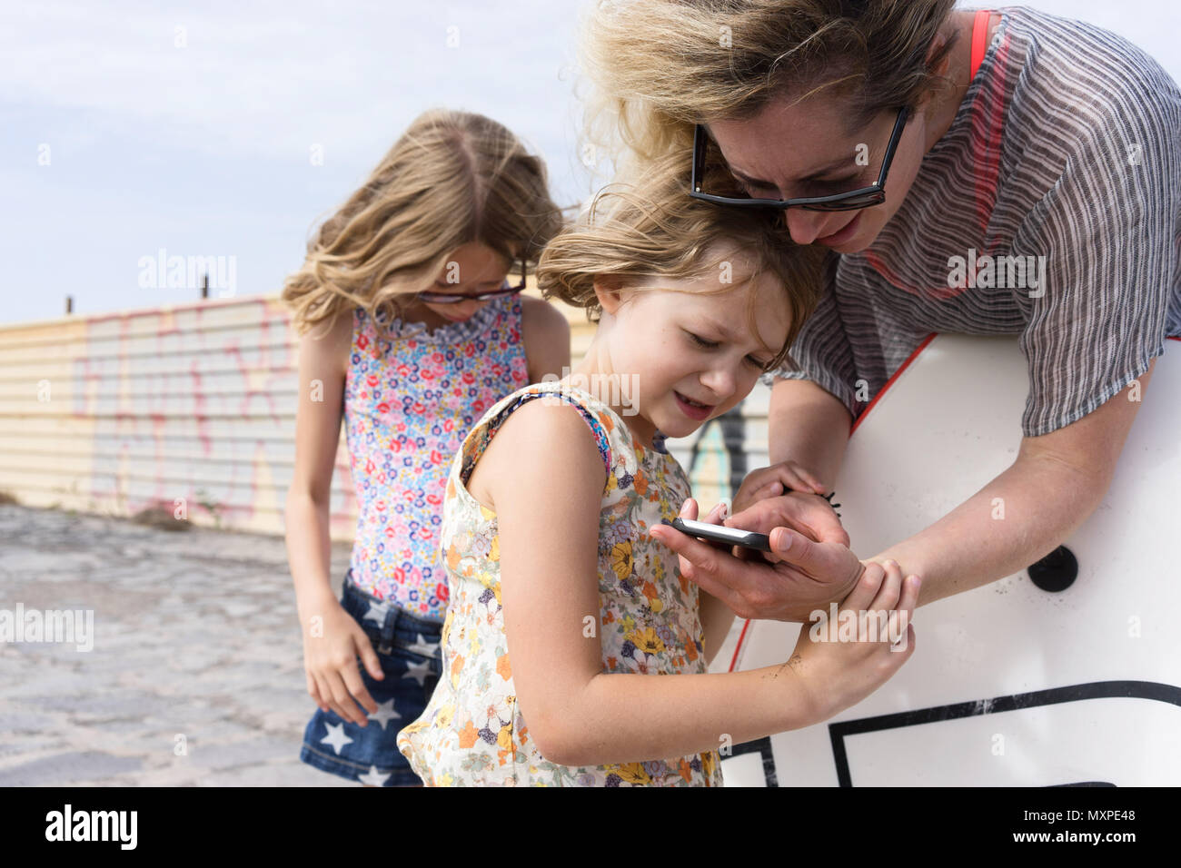 mother showing her daughter something on her mobile phone with the other daughter in the background Stock Photo