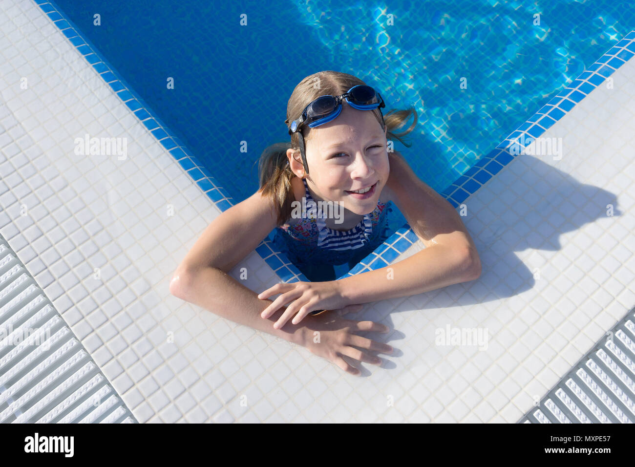 Female child looking up from corner of a swimming pool smiling Stock Photo