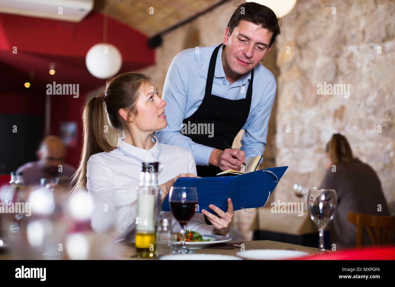 Hospitable waiter helping young girl with menu, taking order in