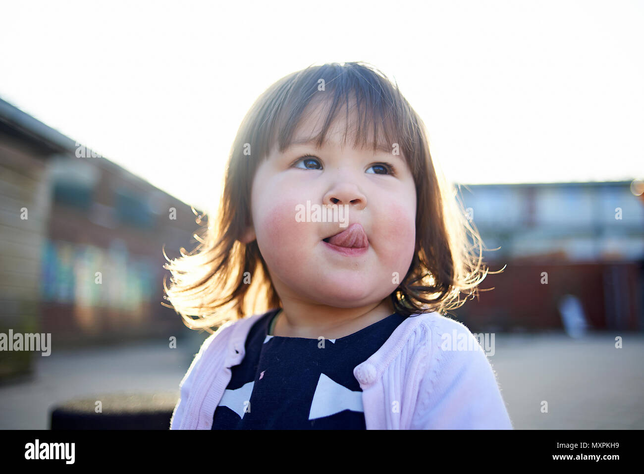 Portrait of a cute young Asian baby girl with rosey cheeks in cold weather sticking out her tongue Stock Photo