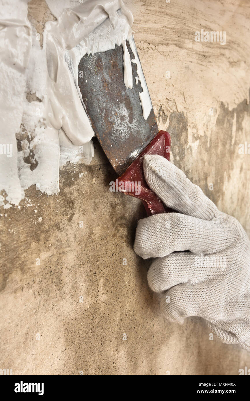hand in glove plastering concrete wall with putty knife during repair