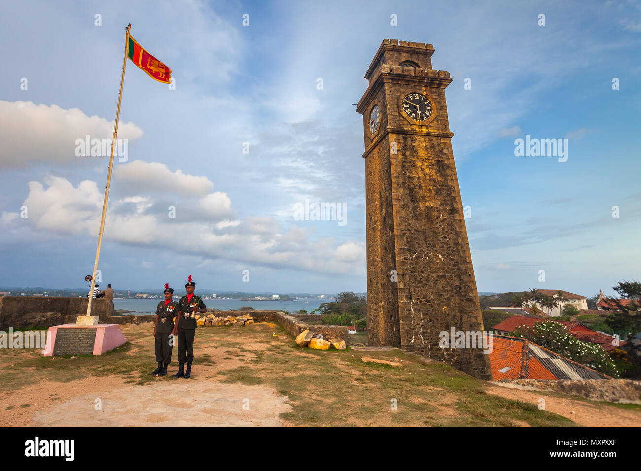 The national symbol of the Democratic Socialist Republic of Sri Lanka the state flag and two soldiers performing the guard of honor next to the clock tower. Galle Fort, UNESCO world heritage site. Stock Photo