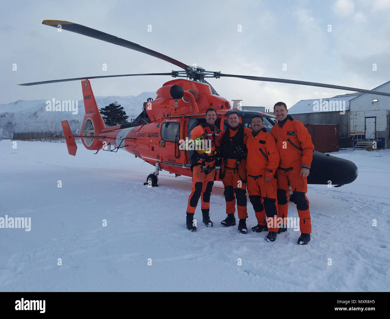Crew members of a Coast Guard Air Station Kodiak MH-65 Dolphin take a photo with two men they rescued after their R22 helicopter crashed near the Dutch Harbor Airport on Unalaska Island, Alaska, Dec. 2, 2016. The helicopter reportedly encountered whiteout conditions and then crashed. U.S. Coast Guard photo by Lt. Craig Hermiller. Stock Photo
