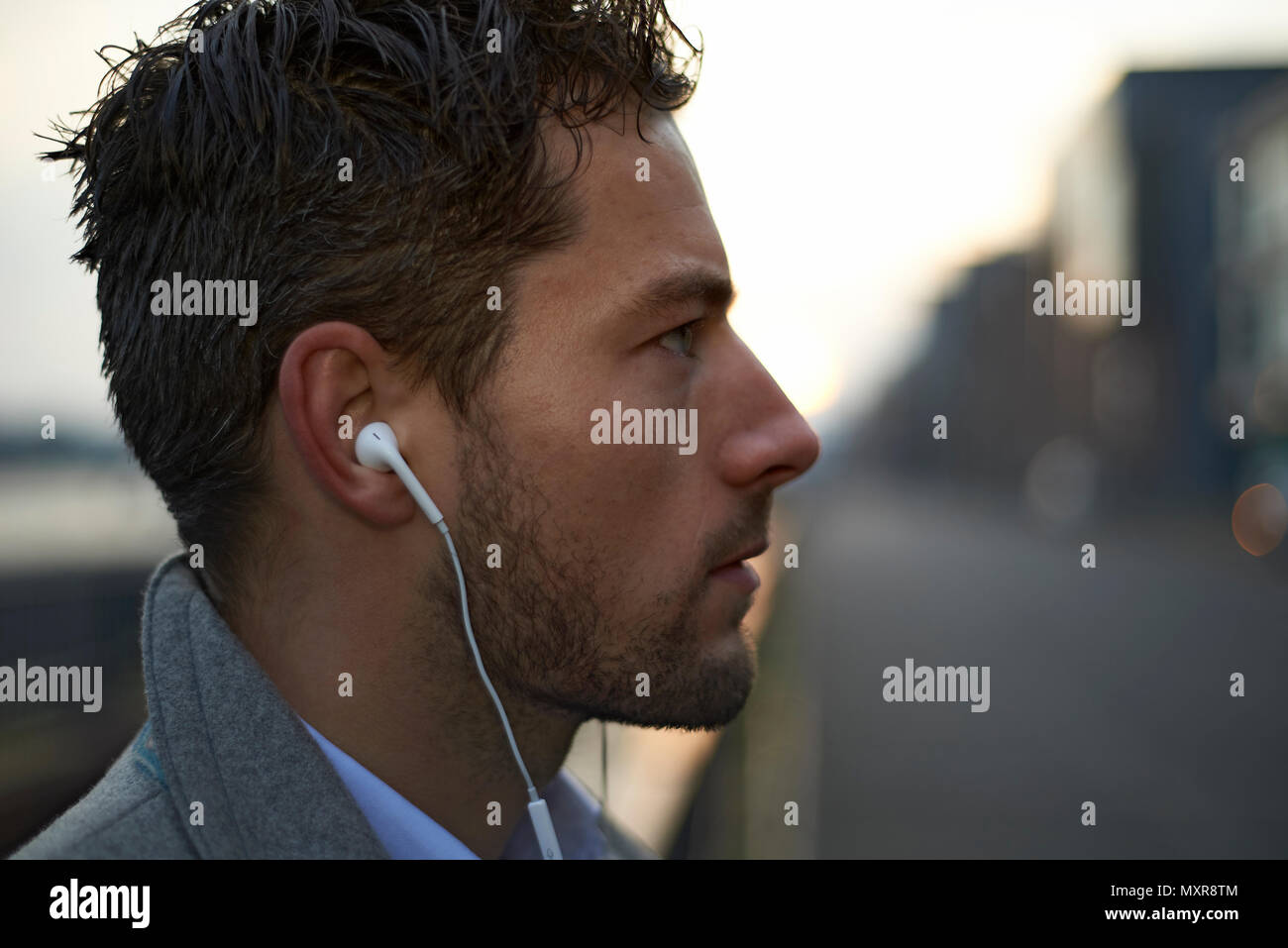 Close up of a well dressed young business man in the city in early morning daylight, the dawning of a new day with new opportunities wearing ear buds Stock Photo