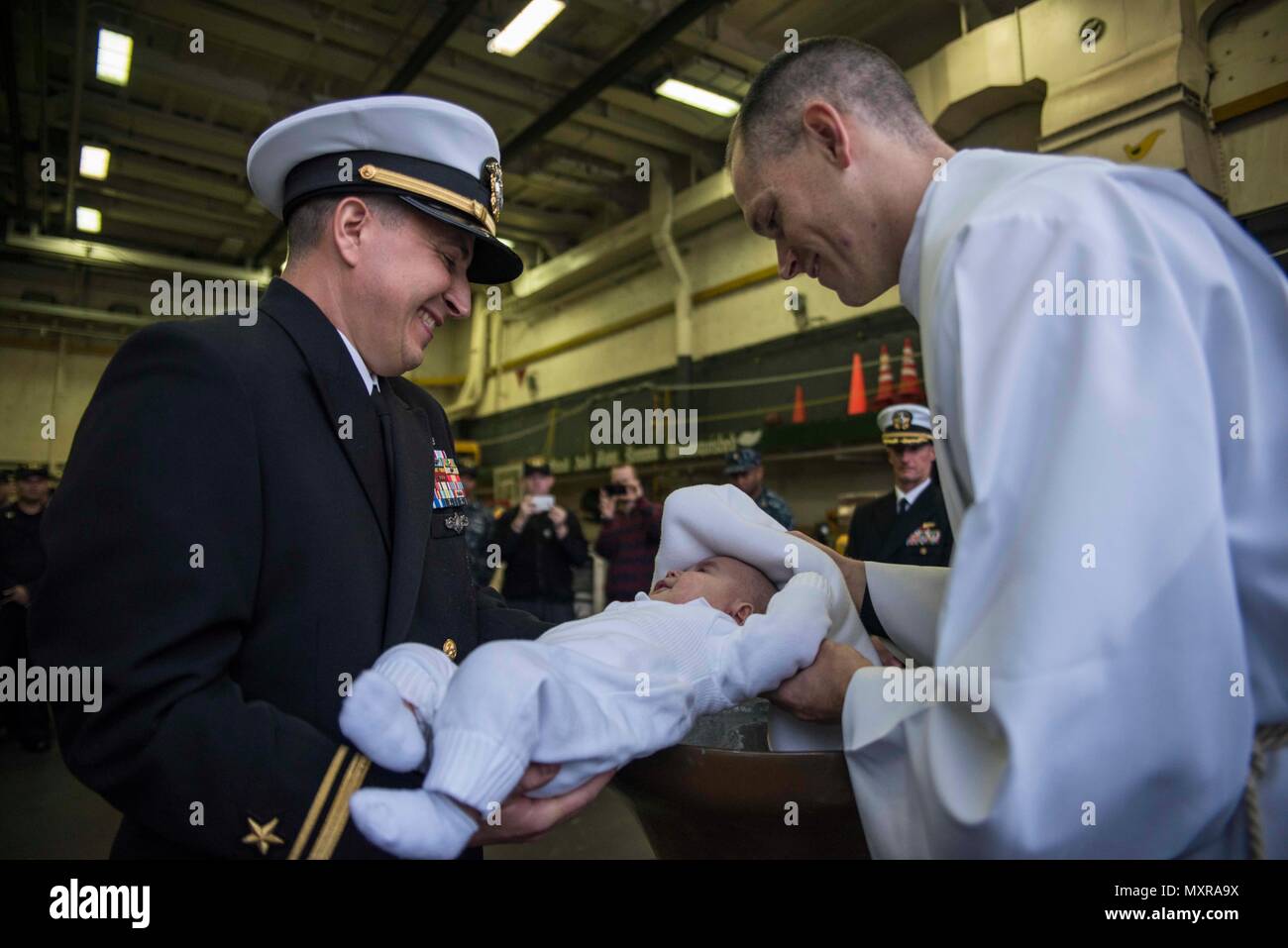 161128-N-JH293-074 SASEBO, Japan (Nov. 28, 2016) Lt. j.g. Brian Caplan has his son baptized in the bell of the amphibious transport dock ship USS Green Bay (LPD 20). Caplan’s son, Theo, was the first newborn to be baptized inside Green Bay’s bell. Conducting baptisms is a Navy tradition that dates back several hundred years to its origins in the British Royal Navy. Green Bay, forward-deployed to Sasebo, Japan, is serving forward to provide a rapid-response capability in the event of a regional contingency or natural disaster. (U.S. Navy photo by Petty Officer 1st Class Chris Williamson/Release Stock Photo