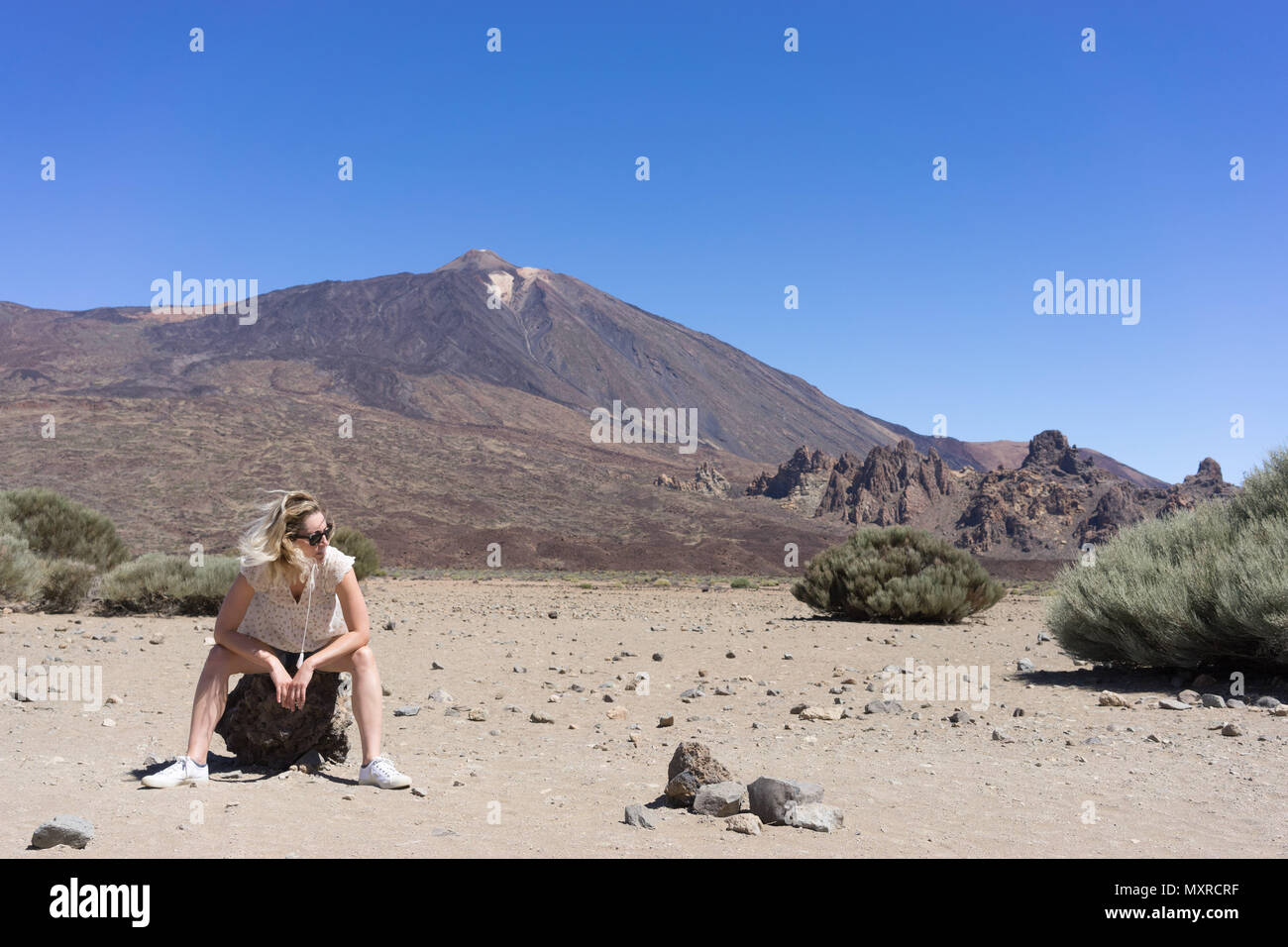 Woman siting on a rock with a volcano in the background Stock Photo