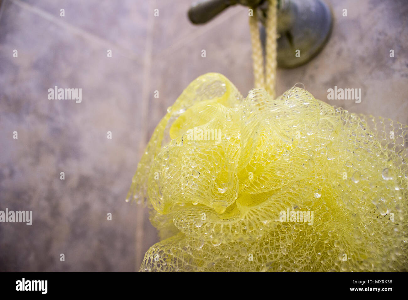 Close-up of a yellow shower puff sponge mesh net ball hanging from a lever handle. Stock Photo