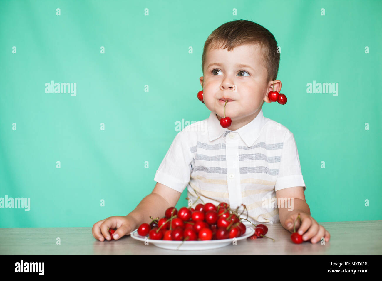 Cute boy boy eating ripe cherries, making funny faces and playing with the cherries, having fun